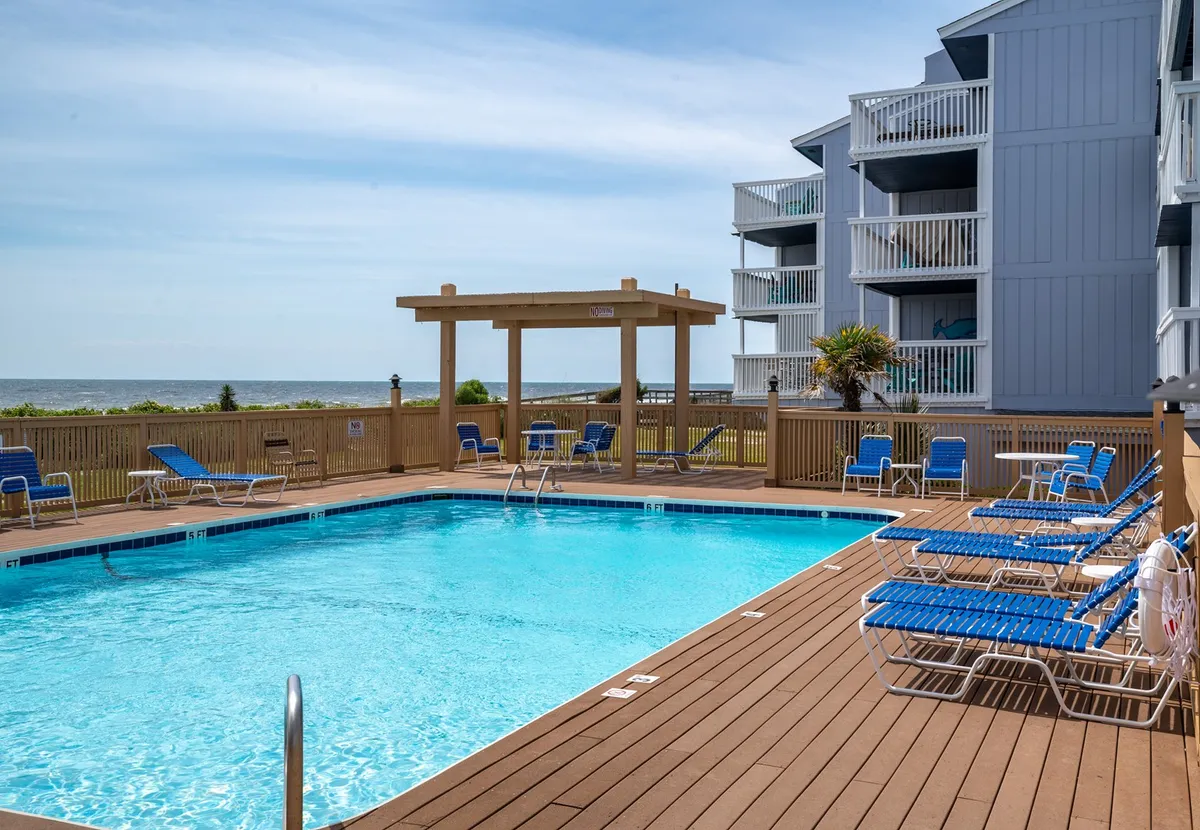 The image showcases a sparkling swimming pool surrounded by plush lounge chairs and a stylish cabana, all set against the backdrop of endless ocean views. The scene evokes a leisurely, upscale atmosphere perfect for swimming, sunbathing, and relaxing with friends or loved ones, with hints of sunset lighting and coastal serenity.