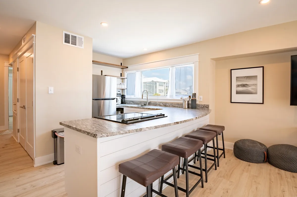 A modern kitchen with an island countertop, bar stools, appliances, and a window that lets in natural light. This open, social space encourages guests to gather, plan their day, and unwind after exploring Carolina Beach.