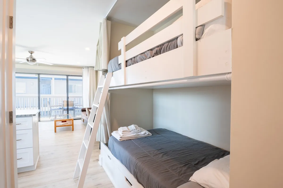 A cozy bunk bed setup occupies a nook, complete with a ladder, neatly made bedding, towels, and a window letting in natural light. The space feels playful, private, and inviting—ideal for children or additional guests.