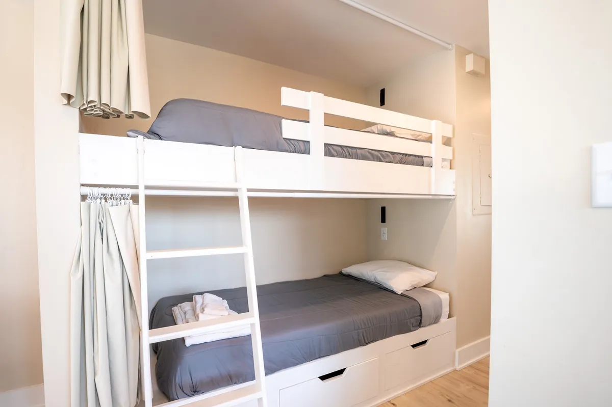 A neatly made, cozy bunk bed with storage drawers and light-colored walls, radiating a sense of warmth and comfort. The space looks perfect for children to unwind after a full day of activities.