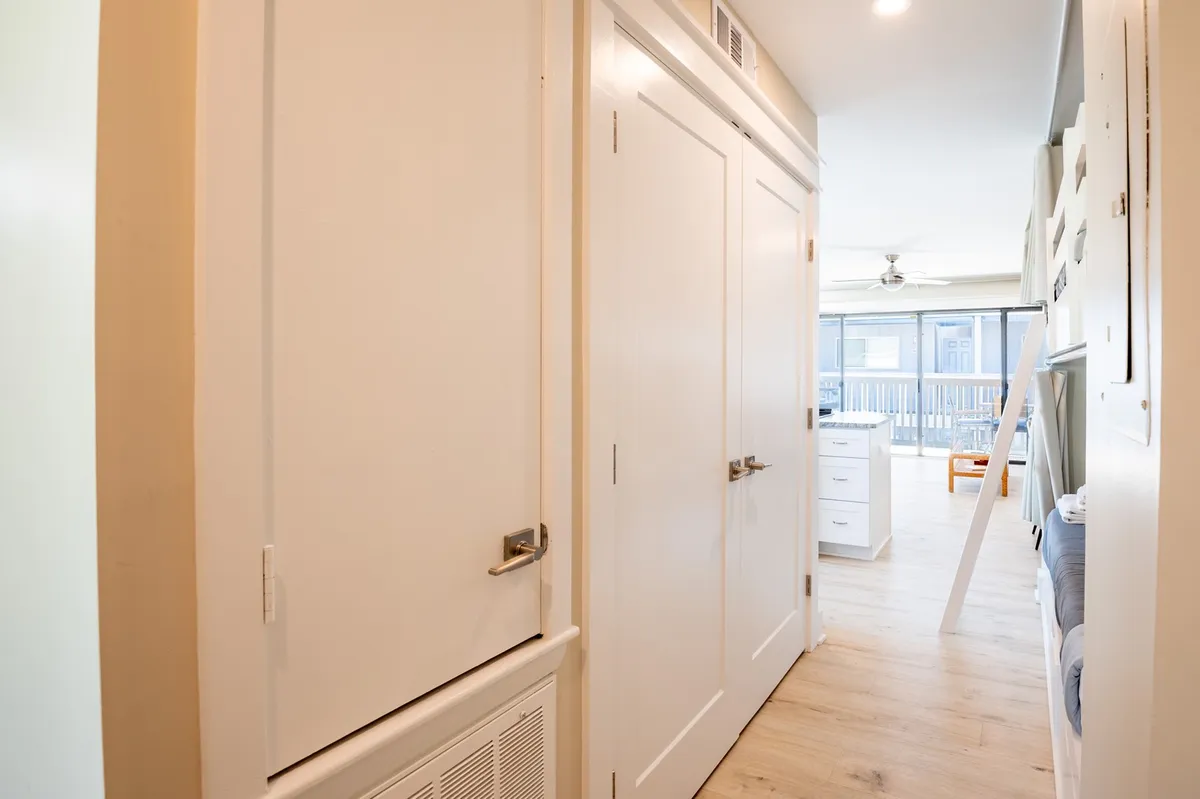 This image showcases a bright, open space with white cabinetry, wooden flooring, and an open door leading directly to the outdoors. The sense of flow between the interior and exterior hints at easy access for families coming and going between pool, beach, and condo.